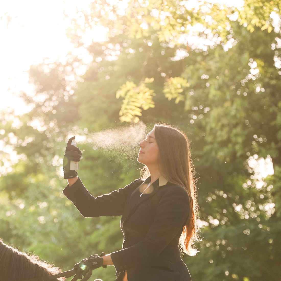 A woman on a horse misting her face with Glisten Up! hydrating, cooling, and anti-inflammatory face mist.