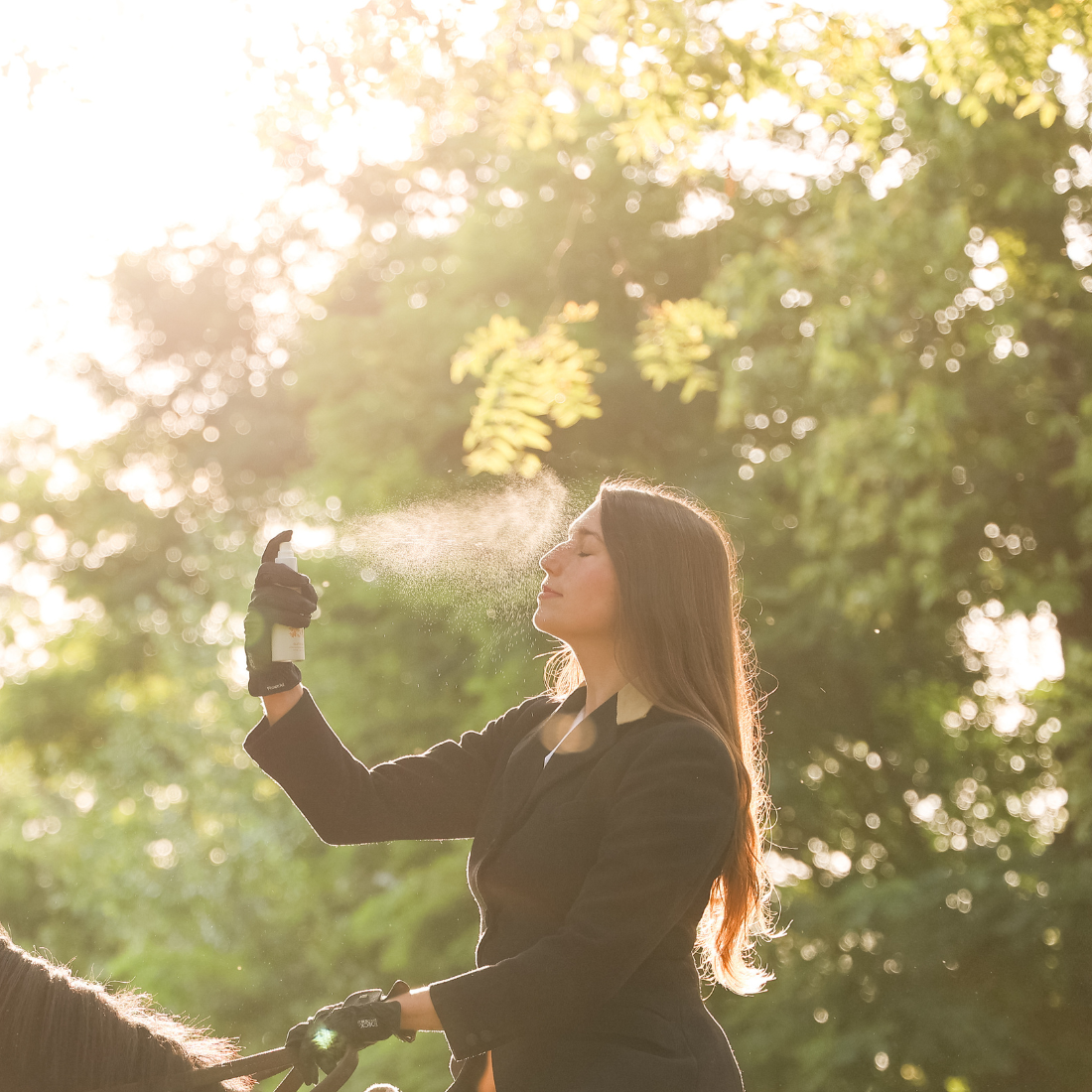 A woman on a horse misting her face with Glisten Up! hydrating, cooling, and anti-inflammatory face mist. 