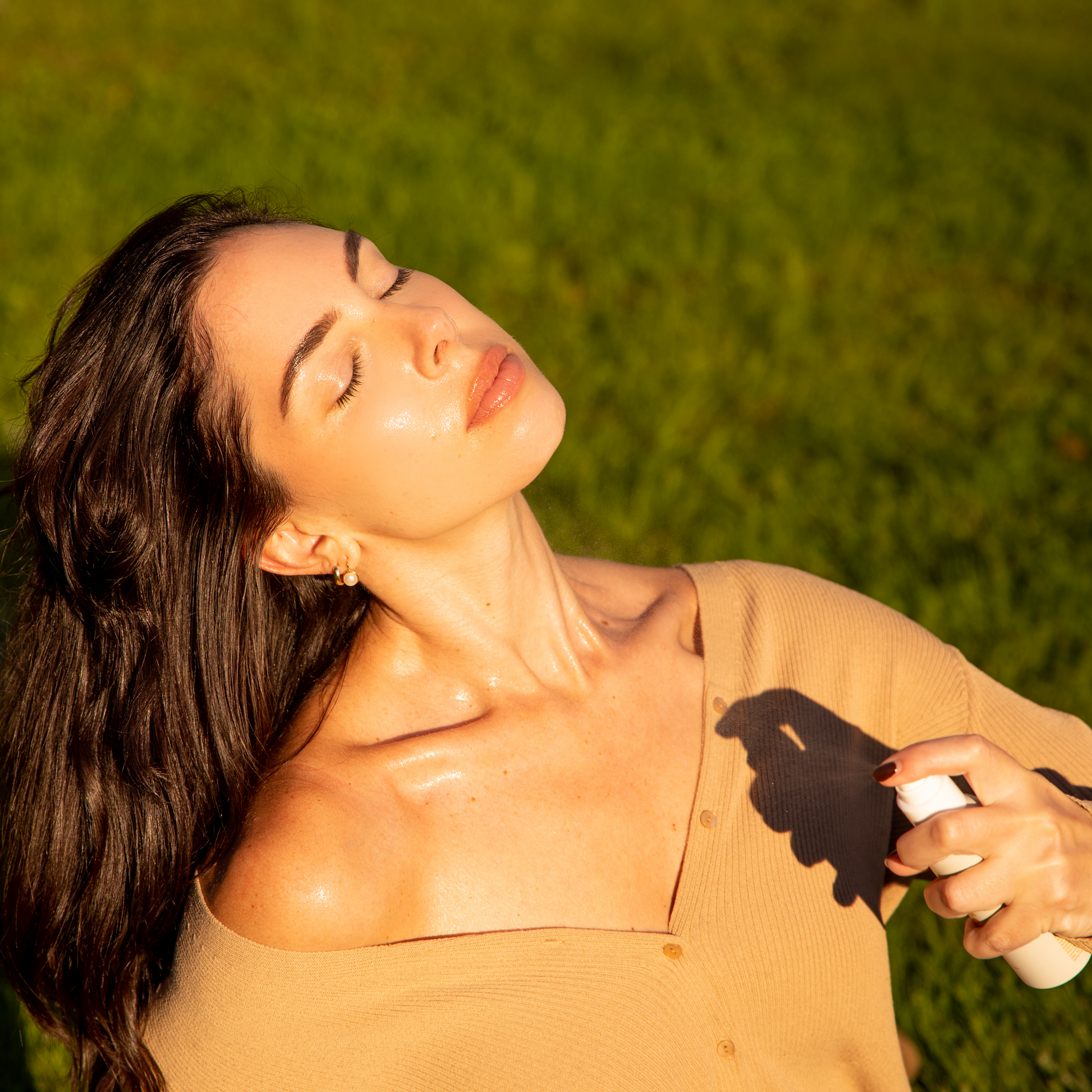 woman lying in the grass misting her face, neck and chest with good psyche glisten up 
