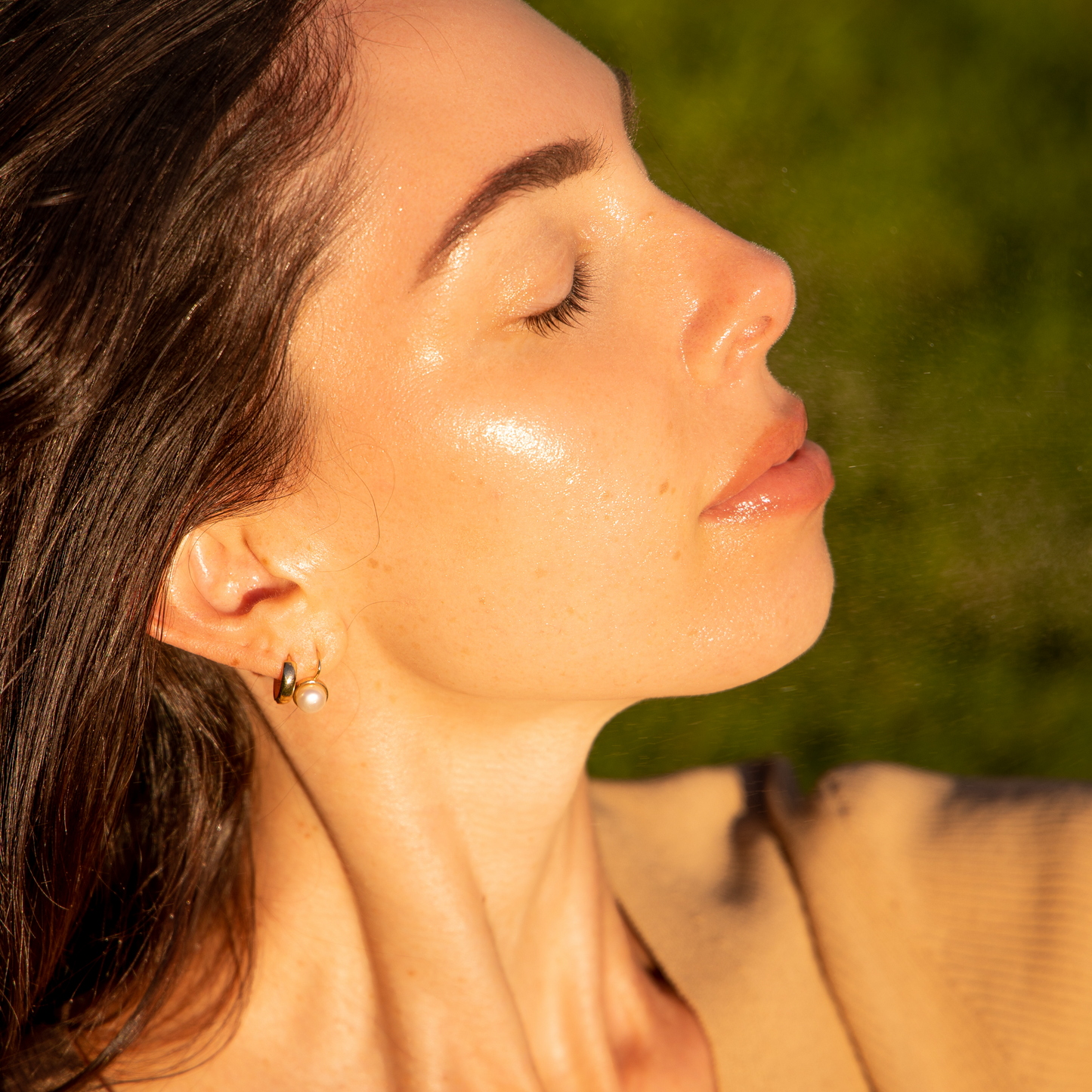 woman with her eyes closed as a delicate mist lands on her dewy hydrated skin